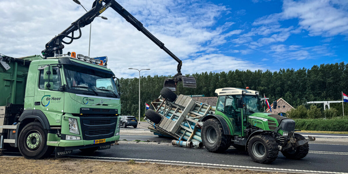 Aanhanger van tractor kantelt: lading buizen op straat